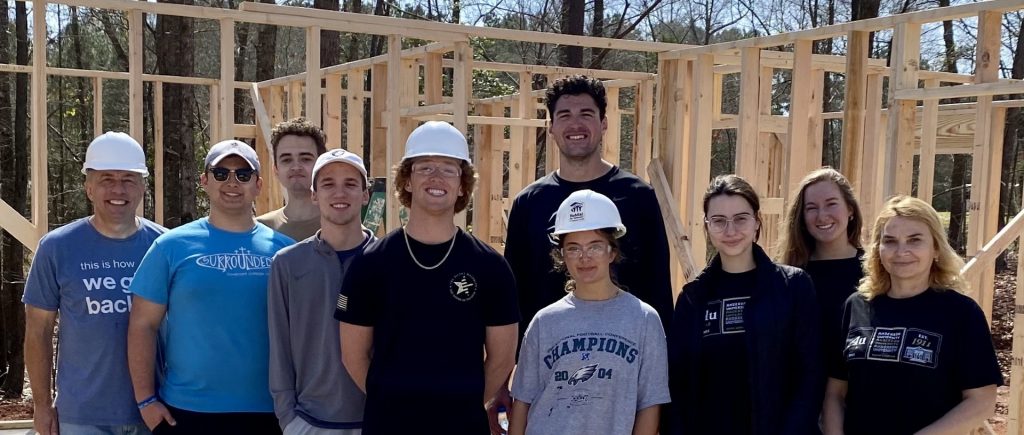 Dr. Mistrean (far right) and Dr. Saunders (far left) along with undergraduate business students framing walls during a Habitat for Humanity workday in March 2024.